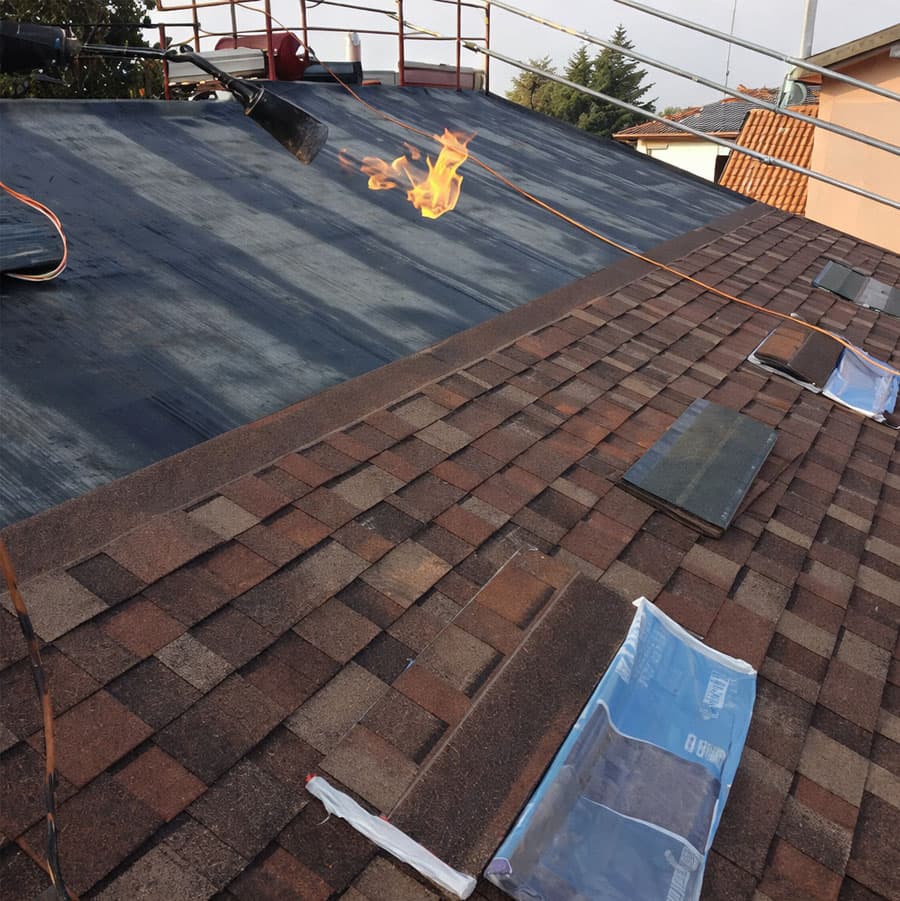 Installazione professionale di una guaina impermeabilizzante bituminosa su tetto: dettaglio della tecnica di fiammatura a caldo per garantire la massima aderenza e tenuta idraulica delle membrane.